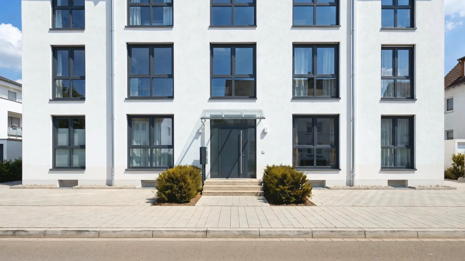 Modernes weißes Mehrfamilienhaus mit sauberem, hellem Gehweg vor der Haustür